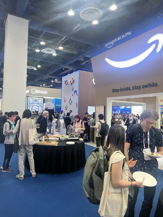 Amazon·Google·Microsoft 부스와 케이터링 테이블이 함께 보이는 전시장.